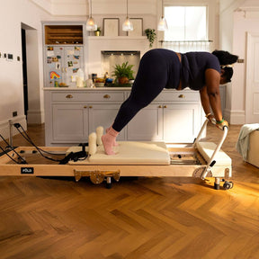 Person using a wooden pilates reformer machine in a home setting